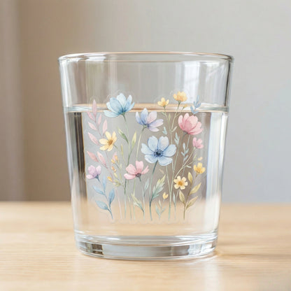 Clear transparent floral sticker applied on glass of water, soft pastel wildflower design with realistic light transmission and seamless transparent edges