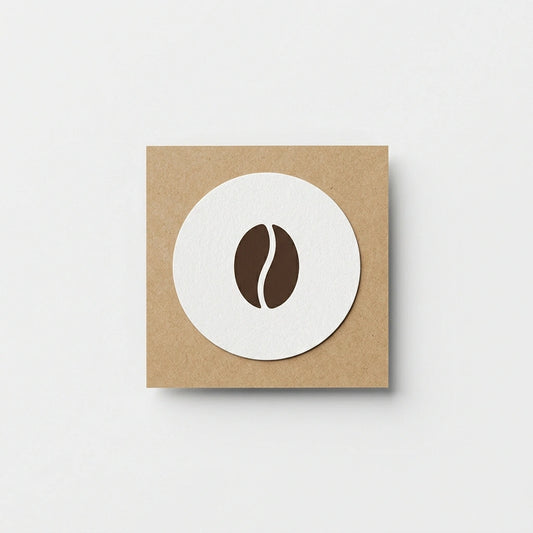 A high-resolution photo of a minimalist, matte white custom round vinyl sticker featuring a small brown coffee bean logo. The sticker is applied to a textured Kraft paper background.